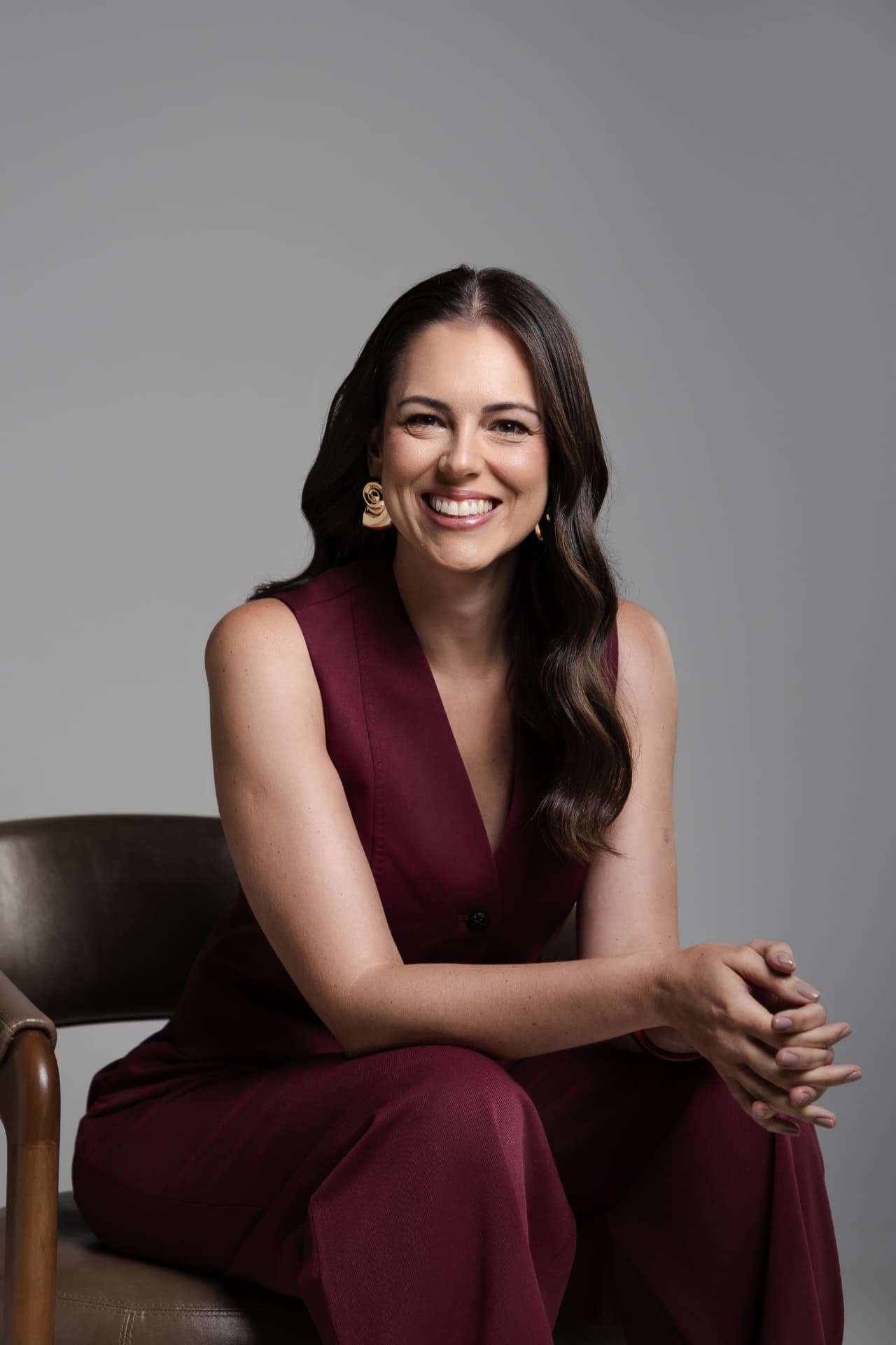 Carol Bellini sentada, sorrindo, vestindo conjunto vinho